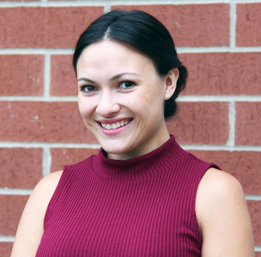 smiling young woman with hair tied back in front of a brick wall