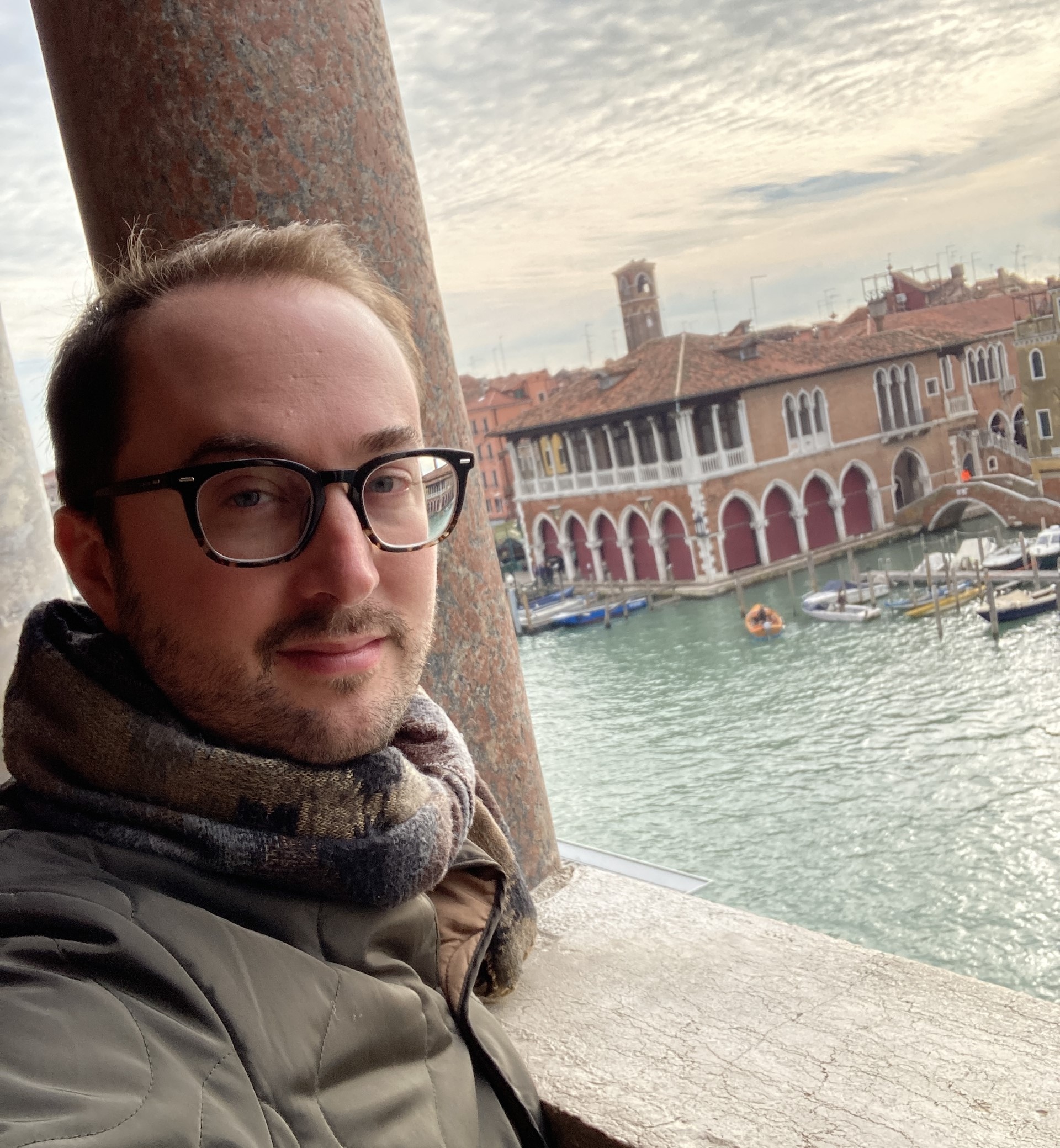 young man with glasses and scarf in front of a river view