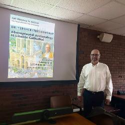 Professor in white shirtsleeves, smiles before presenting a talk on archaeological art history.