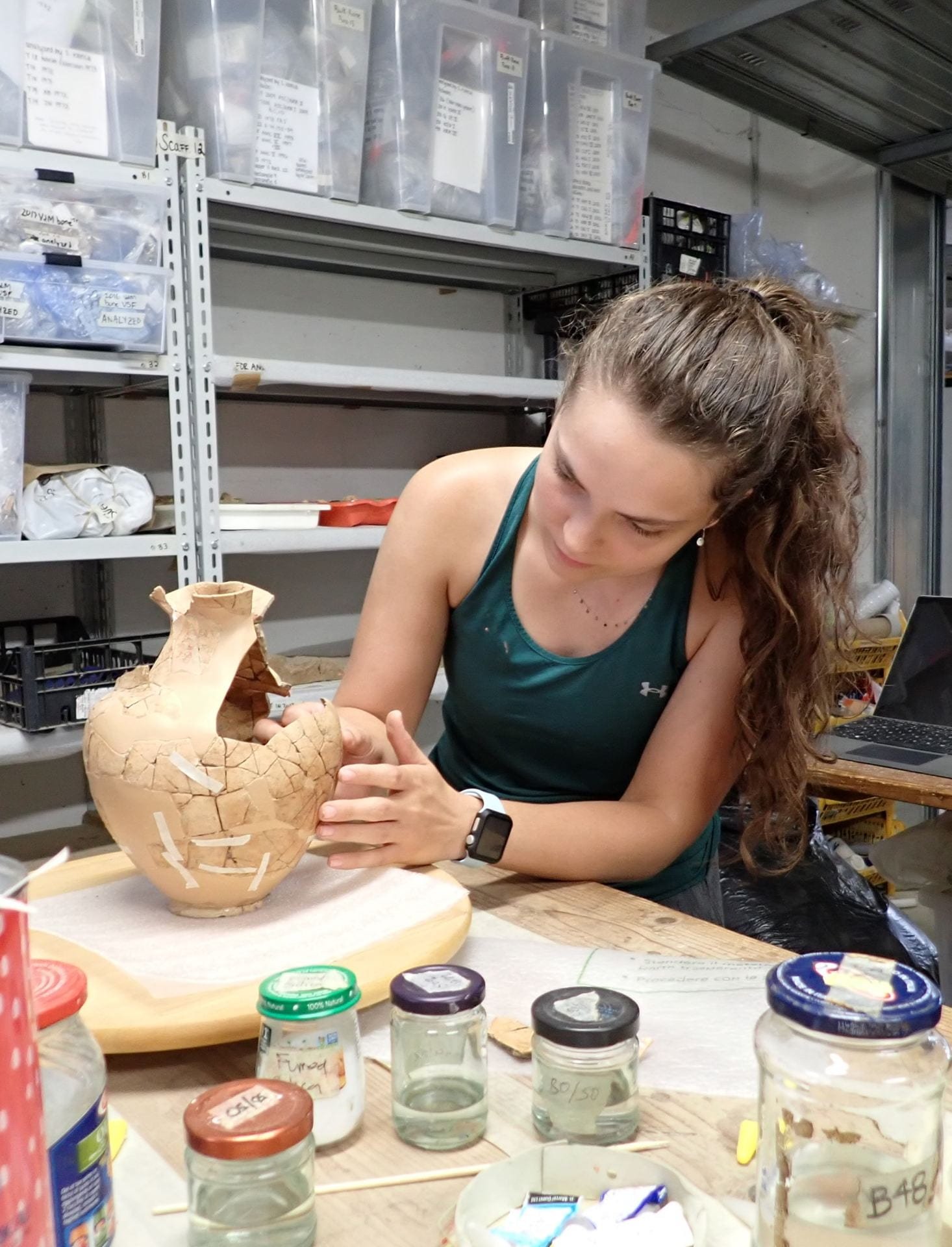 Student in tank top and with long hair, conserving an ancient pot in a lab.