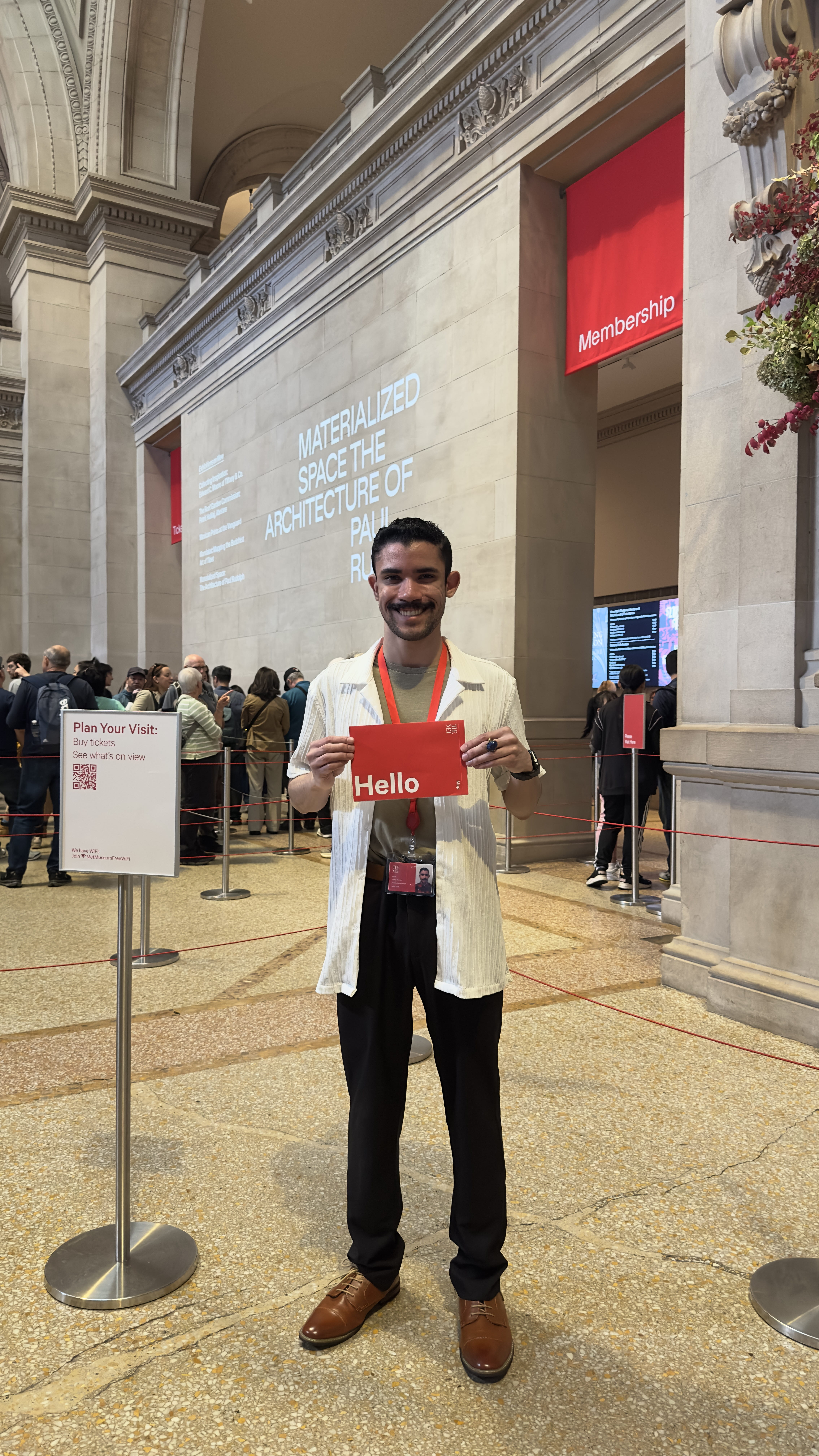 A smiling Met Museum Vistitor Services Staffer, Jorell Herrera New Paltz '23, full length photo in the Great Hall.