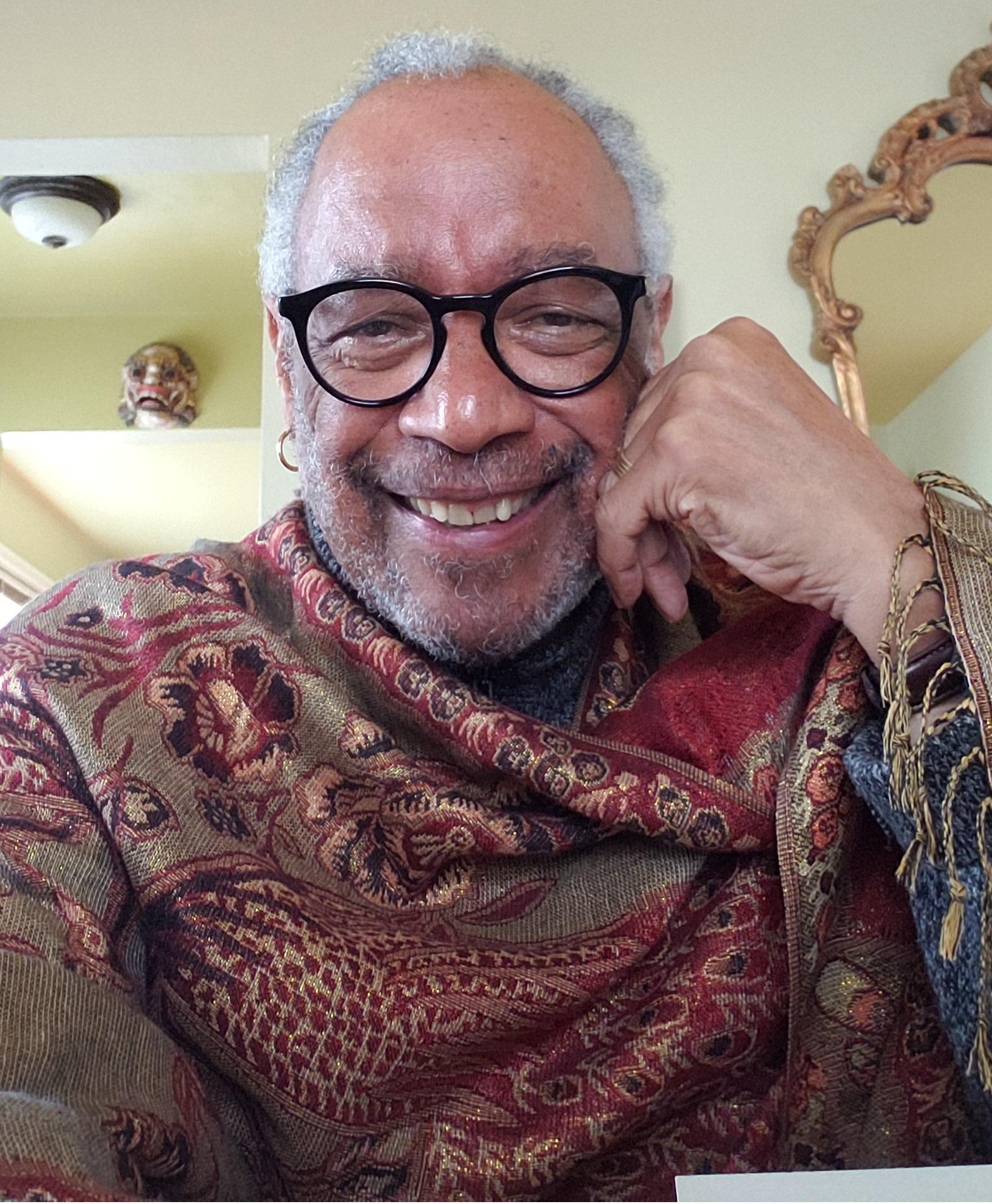 A smiling person, wearing glasses, wrapped in a colorful shawl.