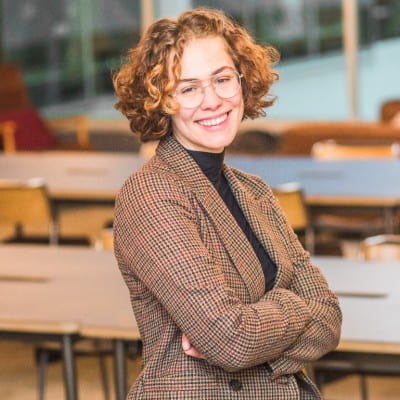 person with short curly hair, glasses and jacket with arms crossed, smiling