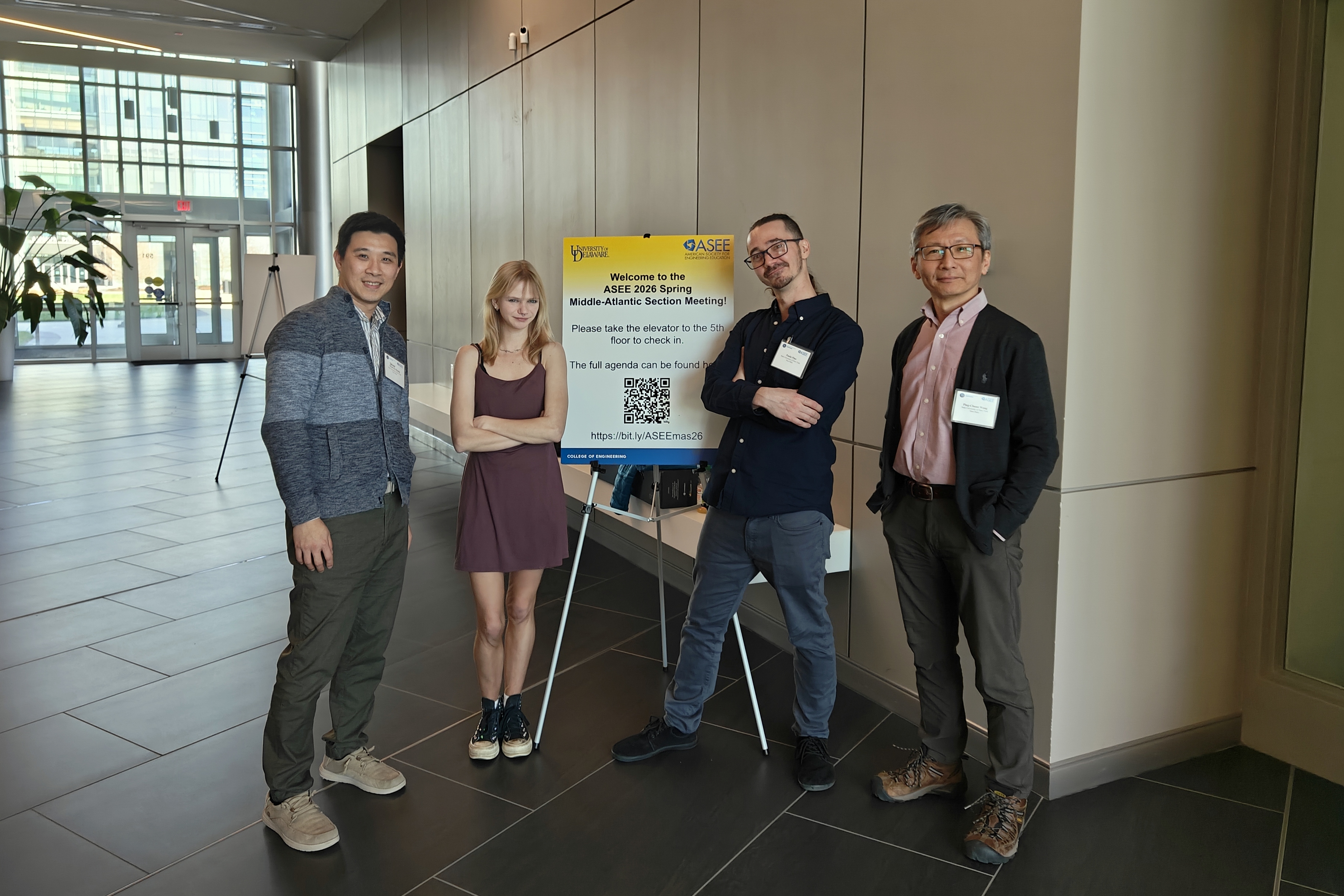 Two students and two faculty members pose in front of a sign for a conference.